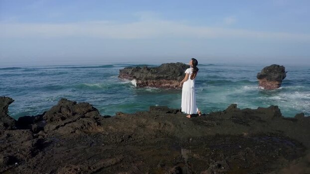 Aerial view of a woman in a white dress on volcanic rocks by the sea Indonesia Aerial view of a woman in a white dress on volcanic rocks by the sea Indonesia