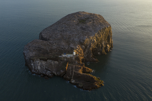 Aerial view of Bass Rock Lighthouse and historic ruins on the steep volcanic island surrounded by the blue waters of the Firth of Forth North Berwick Scotland United Kingdom. Aerial view of Bass Rock Lighthouse and historic ruins on the steep volcanic island surrounded by the blue waters of the Firth of Forth North Berwick Scotland United Kingdom.