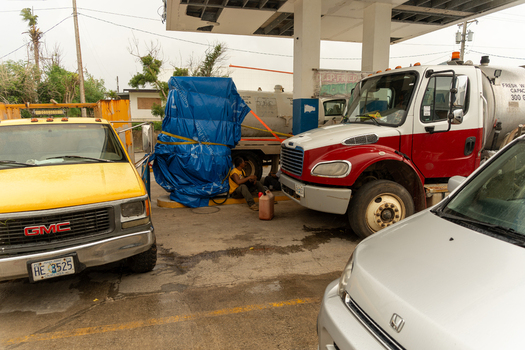 San Jose Tinian Northern Mariana Islands 05 July 2026 View of a gas station with a yellow GMC truck a red and white tanker truck and a person sitting by a blue tarp. San Jose Tinian Northern Mariana Islands 05 July 2026 View of a gas station with a yellow GMC truck a red and white tanker truck and a person sitting by a blue tarp.