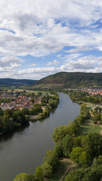 Aerial view of the River Main flowing through the town of Kleinheubach with lush green hills and a blue sky in the background in Kleinheubach Bavaria Germany.