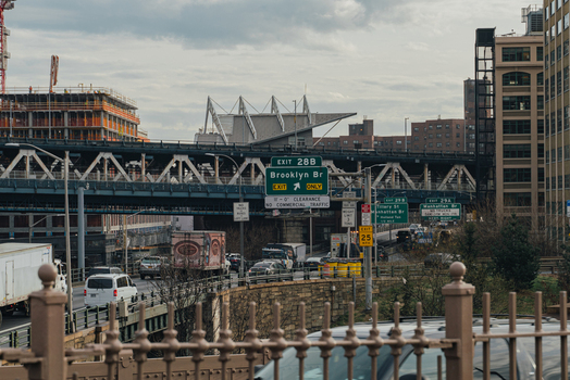 View of the Brooklyn Bridge highway entrance with road signs traffic and urban buildings in the background in New York New York United States.