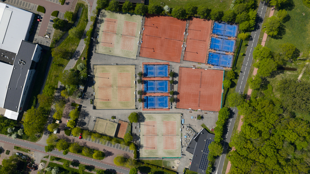 Aerial view of a tennis club featuring multiple clay and hard courts surrounded by lush green trees and adjacent roads in Heiloo North Holland Netherlands.