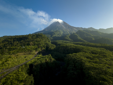 Aerial view of Mount Merapi volcano with smoke rising from the crater above the lush green forests of Bunker Kaliadem Kecamatan Pakem Daerah Istimewa Yogya Indonesia. Aerial view of Mount Merapi volcano with smoke rising from the crater above the lush green forests of Bunker Kaliadem Kecamatan Pakem Daerah Istimewa Yogya Indonesia.