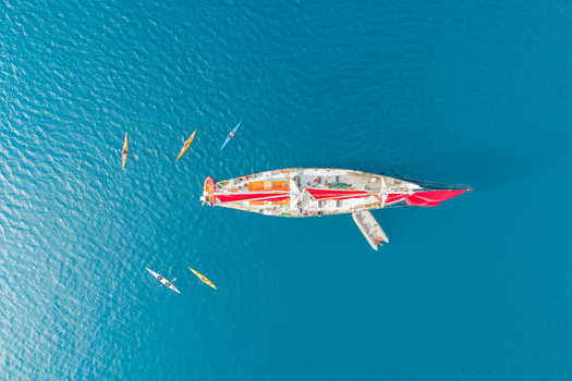 Aerial view of a sailboat with red sails surrounded by several colorful kayaks in the deep blue waters near Uummannaq Kitaa Greenland. Aerial view of a sailboat with red sails surrounded by several colorful kayaks in the deep blue waters near Uummannaq Kitaa Greenland.