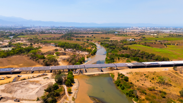 Aerial view of a muddy river and arid plains bisected by a new bridge under construction leading to a distant city Puerto Vallarta Jalisco Mexico.