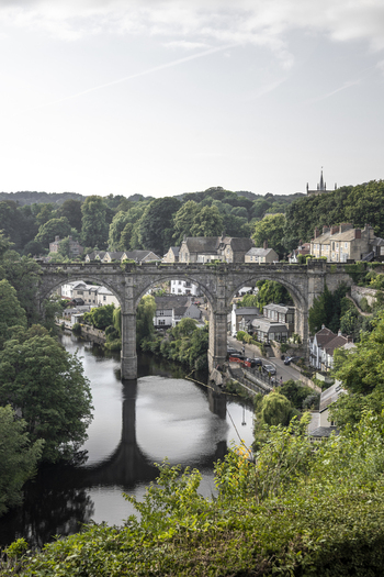 View of the historic Knaresborough Viaduct spanning the River Nidd surrounded by lush trees and stone buildings in Knaresborough England United Kingdom.