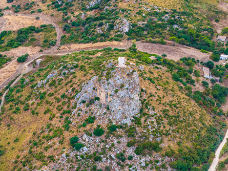 Aerial view of a rocky hill topped with a historic stone watchtower surrounded by Mediterranean scrub dry grass and paths in the rural landscape of Palermo Sicily Italy. Aerial view of a rocky hill topped with a historic stone watchtower surrounded by Mediterranean scrub dry grass and paths in the rural landscape of Palermo Sicily Italy.