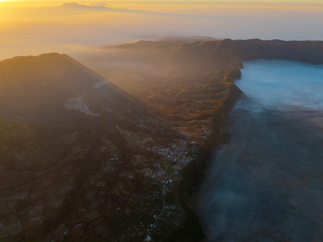 Aerial view of Mount Bromo at sunrise with golden light illuminating the volcanic crater and sea of clouds over the rugged landscape in Tosari East Java Indonesia.