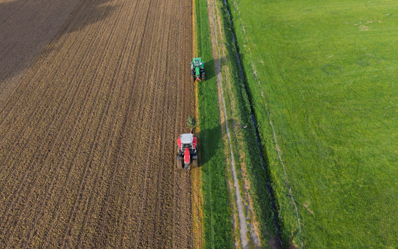 Aerial view of two tractors working on agricultural fields with plowed soil and green grass under bright sunlight Vierpolders South Holland Netherlands. Aerial view of two tractors working on agricultural fields with plowed soil and green grass under bright sunlight Vierpolders South Holland Netherlands.