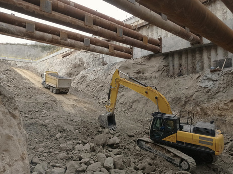 View of a yellow excavator and a dump truck working in a deep excavation pit with large metal support beams overhead in Avcilar Istanbul Turkiye. View of a yellow excavator and a dump truck working in a deep excavation pit with large metal support beams overhead in Avcilar Istanbul Turkiye.