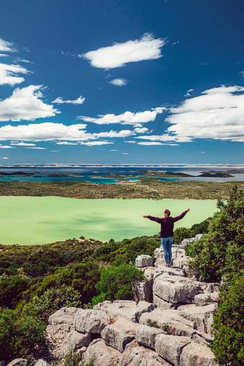 View of a woman with outstretched arms standing on a rocky cliff overlooking Lake Vrana and the Adriatic Sea Vrana Zadar County Croatia. View of a woman with outstretched arms standing on a rocky cliff overlooking Lake Vrana and the Adriatic Sea Vrana Zadar County Croatia.