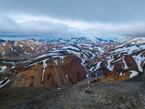 Aerial view of the colorful rhyolite mountains of Landmannalaugar with patches of snow rugged volcanic terrain and dramatic cloudy sky in Rangarthing ytra Iceland. Aerial view of the colorful rhyolite mountains of Landmannalaugar with patches of snow rugged volcanic terrain and dramatic cloudy sky in Rangarthing ytra Iceland.