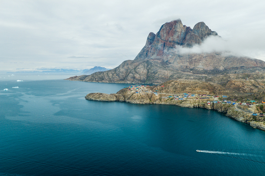 Aerial view of Uummannaq mountain rising above the colorful houses of the coastal town surrounded by deep blue Arctic waters and distant icebergs in Uummannaq Kitaa Greenland. Aerial view of Uummannaq mountain rising above the colorful houses of the coastal town surrounded by deep blue Arctic waters and distant icebergs in Uummannaq Kitaa Greenland.