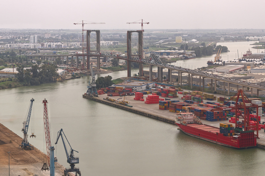 Aerial view of the Puente del Centenario bridge under renovation with construction cranes shipping containers and a red cargo ship at the port in Seville Andalusia Spain.