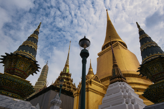 View of the golden spires and ornate architecture of The Grand Palace under a blue sky with scattered clouds in Bangkok Thailand. View of the golden spires and ornate architecture of The Grand Palace under a blue sky with scattered clouds in Bangkok Thailand.