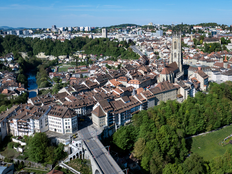 Aerial view of St Nicolas Cathedral towering over the historic old town rooftops Sarine river and Zaehringen bridge under a clear blue sky in Fribourg Fribourg Switzerland. Aerial view of St Nicolas Cathedral towering over the historic old town rooftops Sarine river and Zaehringen bridge under a clear blue sky in Fribourg Fribourg Switzerland.