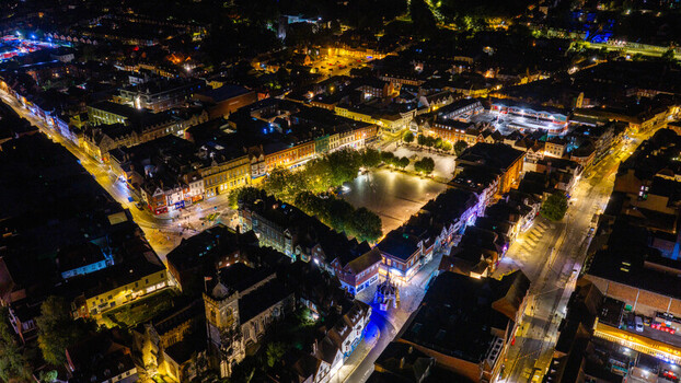Aerial view of the illuminated market square and historic city center at night featuring glowing streetlights and dark rooftops in Salisbury Wilshire United Kingdom. Aerial view of the illuminated market square and historic city center at night featuring glowing streetlights and dark rooftops in Salisbury Wilshire United Kingdom.