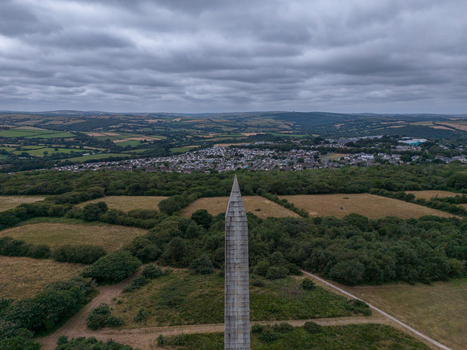 Aerial view of the Bodmin Beacon monument surrounded by lush green fields trees and the town of Bodmin in the distance under a cloudy sky in Bodmin Cornwall United Kingdom. Aerial view of the Bodmin Beacon monument surrounded by lush green fields trees and the town of Bodmin in the distance under a cloudy sky in Bodmin Cornwall United Kingdom.