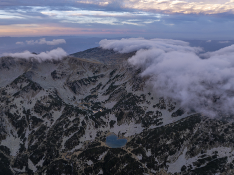 Aerial view of Pirin National Park featuring rugged mountain peaks a heart shaped glacial lake and low hanging clouds over the rocky landscape in Blagoevgrad Province Bulgaria. Aerial view of Pirin National Park featuring rugged mountain peaks a heart shaped glacial lake and low hanging clouds over the rocky landscape in Blagoevgrad Province Bulgaria.