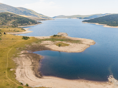 Aerial view of Belmeken Reservoir with its blue waters sandy shoreline and surrounding grassy hills under a clear sky in Pazardzhik Bulgaria. Aerial view of Belmeken Reservoir with its blue waters sandy shoreline and surrounding grassy hills under a clear sky in Pazardzhik Bulgaria.
