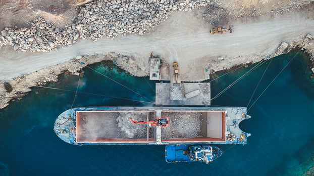Aerial view of a large cargo ship being loaded with white stone at the Jadrankamen quarry with excavators and turquoise water in Pucisca Splitsko dalmatinska Croatia. Aerial view of a large cargo ship being loaded with white stone at the Jadrankamen quarry with excavators and turquoise water in Pucisca Splitsko dalmatinska Croatia.