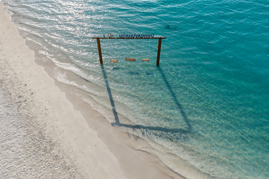 Aerial view of a wooden swing set standing in the turquoise shallow water of a white sandy beach in Kudahuvadhoo Dhaalu Atoll Maldives.