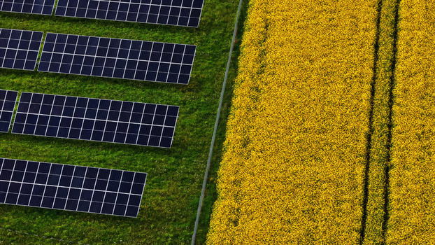 Aerial view of solar panels installed on a green field adjacent to a vibrant yellow rapeseed field in Latvija. Aerial view of solar panels installed on a green field adjacent to a vibrant yellow rapeseed field in Latvija.