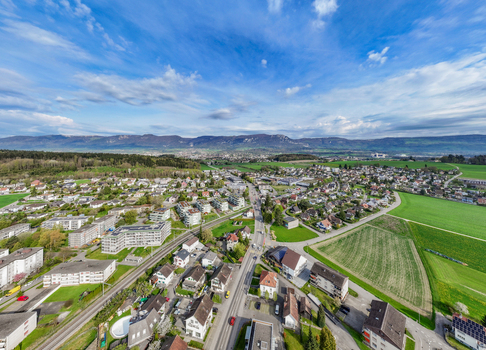 Aerial view of residential houses and lush green fields with the Jura Mountains in the background under a blue sky in Biberist Solothurn Switzerland. Aerial view of residential houses and lush green fields with the Jura Mountains in the background under a blue sky in Biberist Solothurn Switzerland.