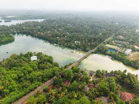 Aerial view of a railway bridge crossing Koggala Lake surrounded by lush tropical palm trees and dense greenery under a hazy sky Koggala Southern Province Sri Lanka. Aerial view of a railway bridge crossing Koggala Lake surrounded by lush tropical palm trees and dense greenery under a hazy sky Koggala Southern Province Sri Lanka.