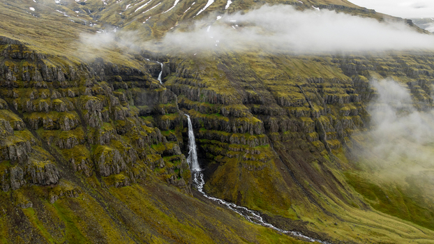 Aerial view of a waterfall cascading down a steep mossy layered cliffside in the Eastern Region of Iceland. Aerial view of a waterfall cascading down a steep mossy layered cliffside in the Eastern Region of Iceland.