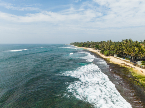 Aerial view of Thalpe Beach featuring turquoise ocean waves crashing against the sandy shore lined with lush palm trees under a bright sky Talpe Southern Province Sri Lanka. Aerial view of Thalpe Beach featuring turquoise ocean waves crashing against the sandy shore lined with lush palm trees under a bright sky Talpe Southern Province Sri Lanka.