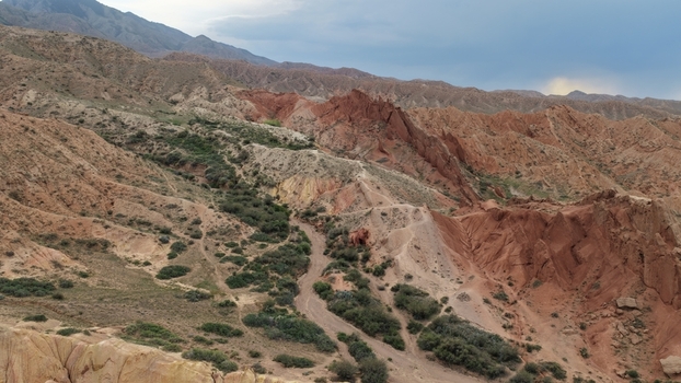 Aerial view of the dramatic red sandstone rock formations of Jety Oguz with green shrubs and a winding trail through the rugged mountain landscape in Jety Oguz Issyk Kul Region Kyrgyzstan. Aerial view of the dramatic red sandstone rock formations of Jety Oguz with green shrubs and a winding trail through the rugged mountain landscape in Jety Oguz Issyk Kul Region Kyrgyzstan.