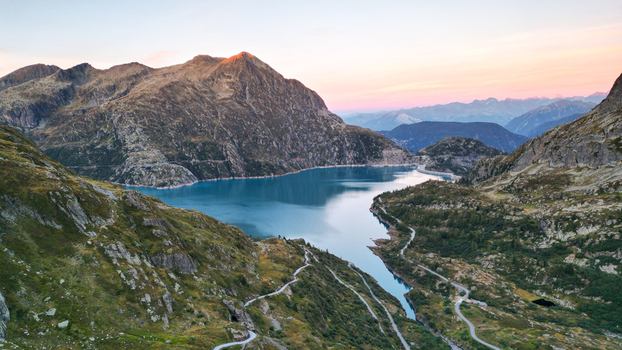 Aerial view of Barrage d Emosson a large dam creating a reservoir with turquoise water surrounded by rugged alpine mountains and winding roads in Finhaut Valais Switzerland.