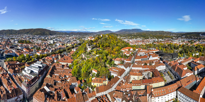 Aerial view of red tiled rooftops cascading across the urban landscape contrasted by the vibrant green foliage and the distant hills Graz Styria Austria.