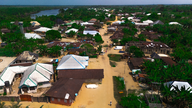 Aerial view of the town of Abua featuring residential houses with metal roofs dirt roads and lush green vegetation surrounded by trees near a river in Abua Rivers Nigeria. Aerial view of the town of Abua featuring residential houses with metal roofs dirt roads and lush green vegetation surrounded by trees near a river in Abua Rivers Nigeria.