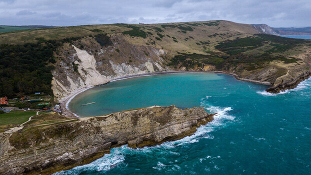 Aerial view of Lulworth Cove a horseshoe shaped bay with turquoise waters dramatic limestone cliffs and rolling green hills United Kingdom.