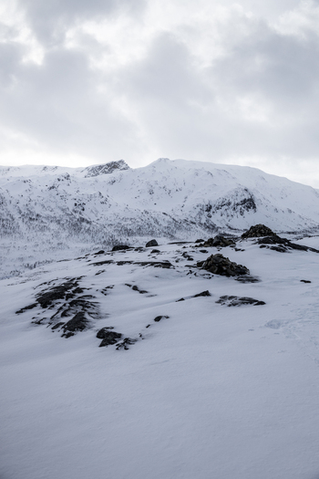 View of snow covered mountain peaks under a dramatic cloudy sky with rocky outcrops in the foreground Ersfjord Troms Norway. View of snow covered mountain peaks under a dramatic cloudy sky with rocky outcrops in the foreground Ersfjord Troms Norway.