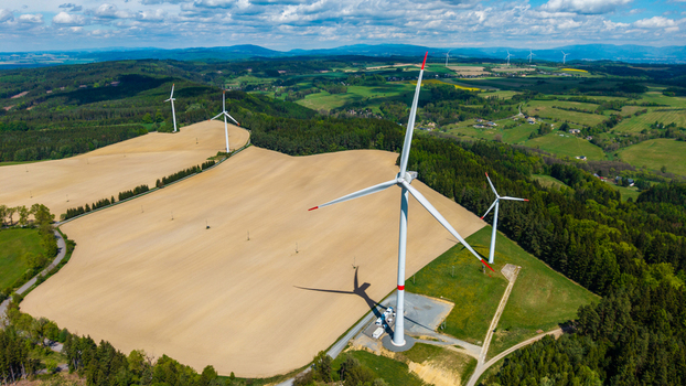 Aerial view of wind turbines at Zipotin standing over rolling agricultural fields and lush green forests under a blue sky in Gruna Pardubicky kraj Czechia. Aerial view of wind turbines at Zipotin standing over rolling agricultural fields and lush green forests under a blue sky in Gruna Pardubicky kraj Czechia.