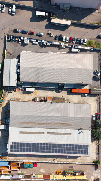 Aerial view of a chemical plant with industrial buildings rooftop solar panels parking areas with cars and storage containers in Milan Lombardy Italy.