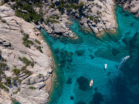 Aerial view of turquoise waters and rocky coastline with small boats floating in the clear sea in San Teodoro Sardegna Italy.