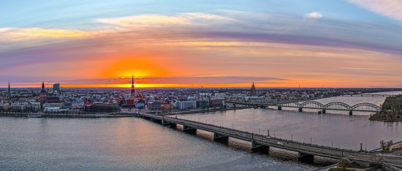 Aerial view of the historic Riga skyline at sunset with the Daugava River and bridges under a vibrant orange sky in Riga Latvia.