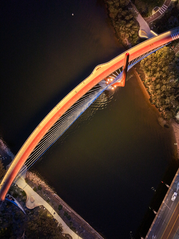 Aerial view of Boorloo Bridge illuminated at night spanning the water with vibrant orange lighting surrounded by dark pathways and lush greenery East Perth Western Australia Australia.
