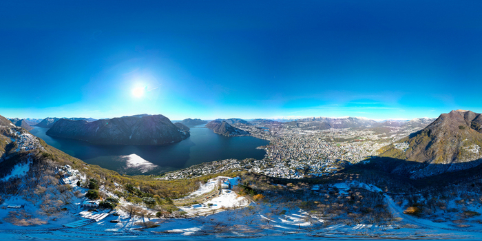 Aerial view of Monte Bre overlooking Lake Lugano and the city skyline with snow dusted mountains under a bright sun in Lugano Ticino Switzerland.