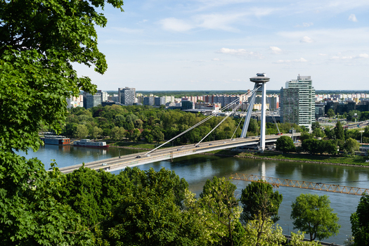 View of the Most SNP bridge with its iconic UFO observation deck crossing the Danube river surrounded by lush greenery and the city skyline Bratislava Bratislava Region Slovakia. View of the Most SNP bridge with its iconic UFO observation deck crossing the Danube river surrounded by lush greenery and the city skyline Bratislava Bratislava Region Slovakia.