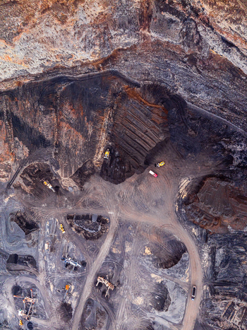 Aerial view of an open pit mine with heavy machinery excavators and trucks operating on dark earth and gravel tracks in Iceland. Aerial view of an open pit mine with heavy machinery excavators and trucks operating on dark earth and gravel tracks in Iceland.