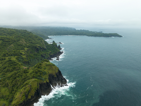 Aerial view of the rugged Pengilon Hill coastline where verdant cliffs meet the turquoise sea Gunungkidul Regency Daerah Istimewa Yogyakarta Indonesia. Aerial view of the rugged Pengilon Hill coastline where verdant cliffs meet the turquoise sea Gunungkidul Regency Daerah Istimewa Yogyakarta Indonesia.