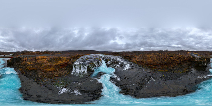 Aerial view of Bruarfoss waterfall with turquoise blue water flowing over dark volcanic rock formations under a cloudy sky in Blaskogabyggd Blaskogabyggd Iceland.