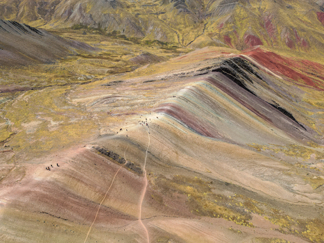 Aerial view of Vinicunca the Rainbow Mountain showing its vibrant mineral stripes and hikers on the ridge trail in the Andes Quispicanchi Province Cusco Peru.