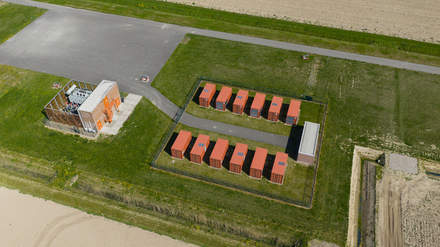 Aerial view of the Energiepark Haringvliet Zuid battery storage facility with orange containers and a transformer station surrounded by green fields in Middelharnis South Holland Netherlands.
