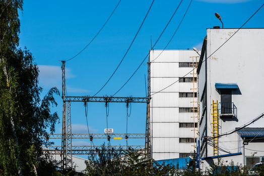 View of electrical power lines and a tall industrial building with a white facade under a clear blue sky in Poland.